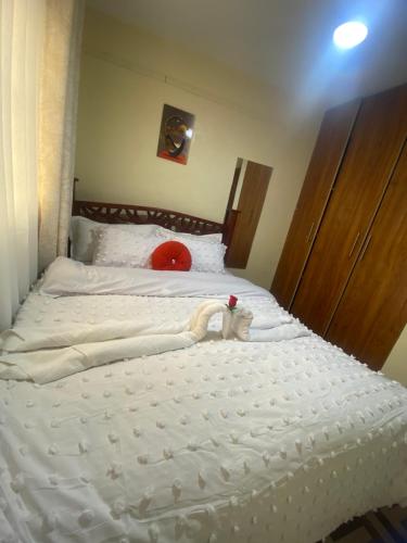 Una cama con sábanas blancas y un sombrero rojo encima. en Urbano roost Ruiru Kamakis , home away from home a comfortable place to cool and unwind after a busy day, en Nairobi