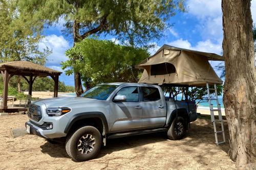 a silver truck parked next to a tree with a tent at Kauai Explorer Rooftop Camper Drive, Camp & Relax in Anahola