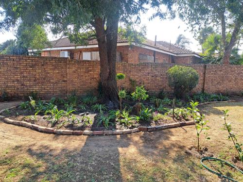 a garden with a tree in front of a brick wall at Dragonfly in Boksburg