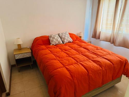 a bed with an orange comforter in a bedroom at Dpto céntrico VGB in Villa General Belgrano