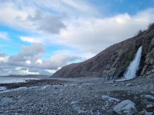 a waterfall on the side of a mountain next to the ocean at Rose's Studio, Bucks Mills in Bideford