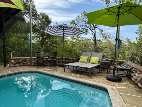 a swimming pool with chairs and umbrellas next to a patio at The Rivery Retreat, Choose from Luxury Guesthouse Cabin OR Poolside Suite in Lake Austin Hill Country in Austin