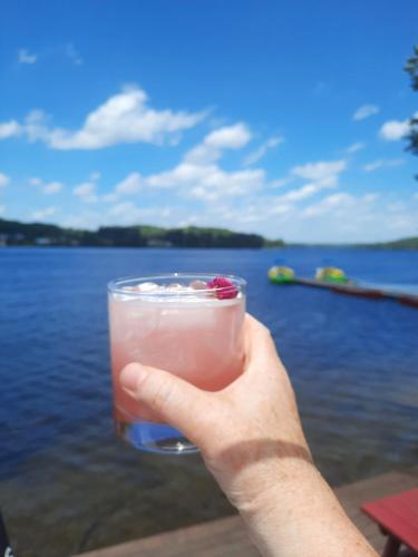 a hand holding a drink in front of a lake at Bonnie View Inn in Haliburton
