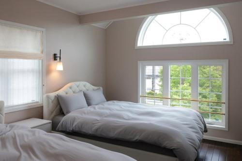 Un dormitorio con dos camas y dos ventanas. en 軽井沢の森に佇む英国様式白の宮殿 薪ストーブある5ldk ポーラーリゾート軽井沢ミューズ, en Naganohara