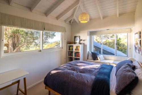 a bedroom with a bed and a desk and two windows at Palm Beach Retreat - Be My Guest Waiheke in Waiheke Island