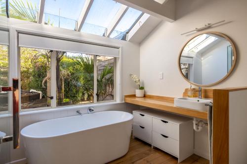 a bathroom with a large white tub and a window at Palm Beach Retreat - Be My Guest Waiheke in Waiheke Island