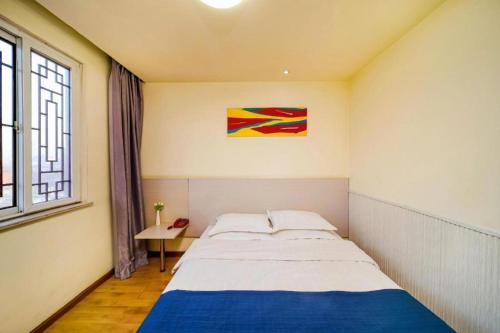 a bedroom with a bed and a painting on the wall at Kunlun Leju Business Hotel Kaifeng Gulou in Kaifeng