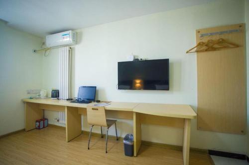 a room with a desk with a laptop and a tv on the wall at 7 Days Inn Jinan Changqing Jingshi West Road Center in Jinan