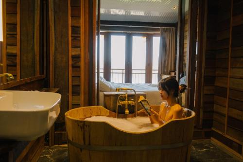 Una mujer en una bañera de madera en un baño con lavabo. en Suneta Hotel Chiangkhan Soi 6, en Chiang Khan