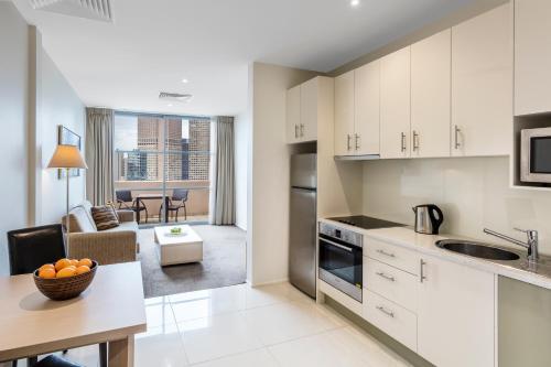 a kitchen with white cabinets and a living room at Oaks Melbourne on Lonsdale Suites in Melbourne