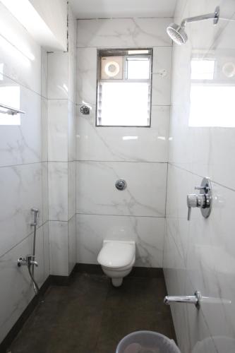 a white bathroom with a toilet and a window at Vasantharaja Inn in Puducherry