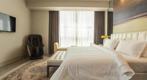 a bedroom with a large white bed and a chair at Jinjiang Metropolo Hotel - Turpan Administration Center in Turfan
