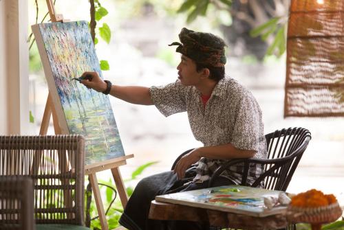 a man sitting in front of a painting on a table at Grandmas Plus Hotel Seminyak in Seminyak