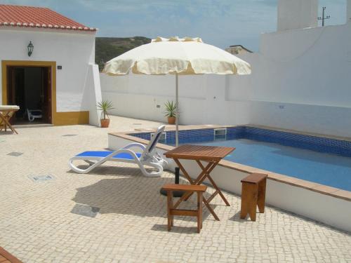 a pool with an umbrella and a table and a chair at Carrapateiramar Guest House in Carrapateira