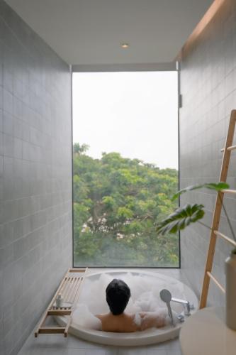 a man laying in a bath tub with a window at Riva Vista Riverfront Resort Chiang Rai in Chiang Rai