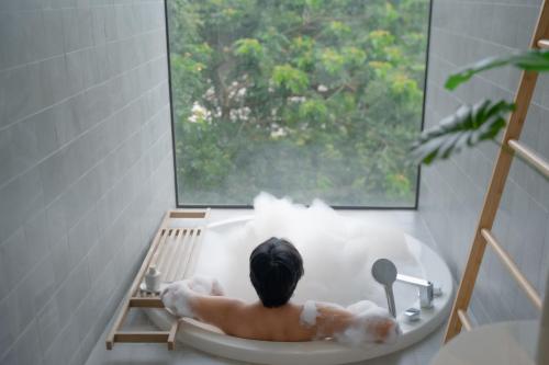 a man sitting in a bath tub looking out a window at Riva Vista Riverfront Resort Chiang Rai in Chiang Rai