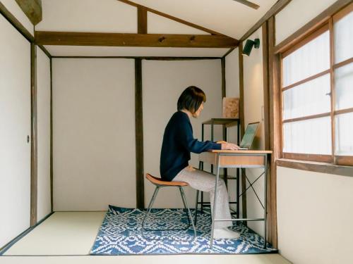 eine Frau, die mit einem Laptop an einem Schreibtisch in einem Raum sitzt in der Unterkunft Kominka Hotel kurasu - Vacation STAY 24275v in Tatsuno