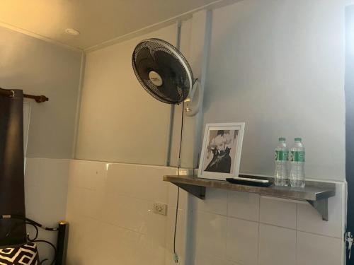 a room with a fan and a shelf with bottles at Cat in the box homestay in Godown