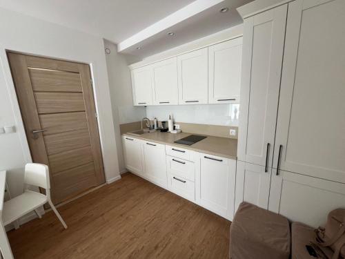 a kitchen with white cabinets and a wooden floor at Apartamenty nad jeziorem Nyskim - Orzechowa 22 in Skorochów
