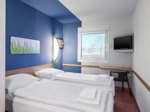 a room with two beds and a tv and a window at B&B HOTEL Düsseldorf-Hilden in Hilden