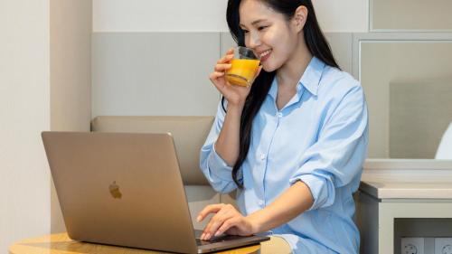 a woman sitting at a table with a laptop and a glass of juice at Browndot Hotel Jeonju Junghwasan in Jeonju