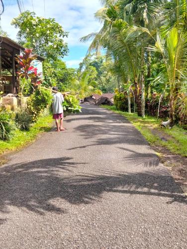 a woman walking down a road with palm trees at Nostalgia Camping Home in Selemadeg
