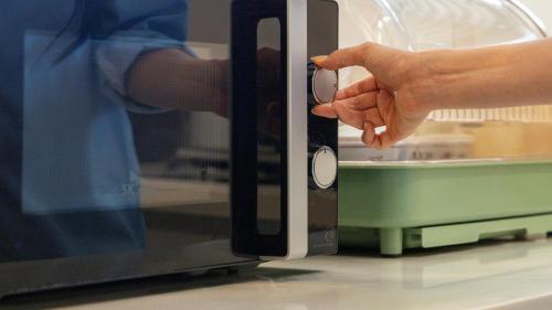 a person holding the door of a microwave at Browndot Hotel Jeonju Junghwasan in Jeonju