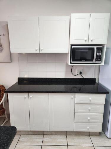 a kitchen with white cabinets and a microwave at Driftsands Sea View Flats in Uvongo Beach