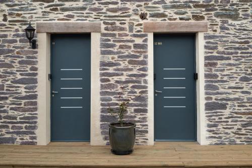 two blue doors on a stone building with a potted plant at La Loge du Roi Arthur in Campénéac