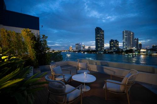a balcony with chairs and tables and a view of the city at The Salil Hotel Riverside Bangkok in Bangkok
