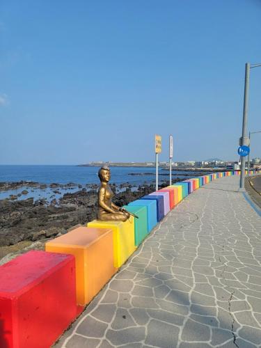 a statue sitting on a colorful bench next to the beach at Oh Happy Day Jeju in Jeju