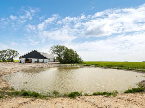 a pond in the middle of a field with a barn at Holiday Home Guthorm by Interhome in Højer