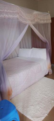 a bedroom with a canopy bed with white sheets and pillows at Hotel Judith, GULU in Buwate