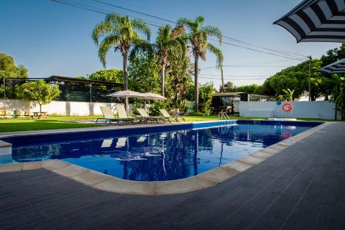a swimming pool with chairs and an umbrella and palm trees at WOT Algarve in Almancil