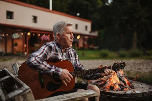 a man playing a guitar next to a fire at Uroczysko Oleśnica in Chodzież