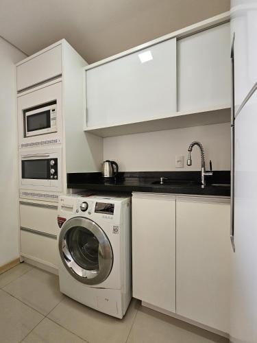 a kitchen with a washing machine and a microwave at Loft Centro Oktoberfest - Blumenau in Blumenau