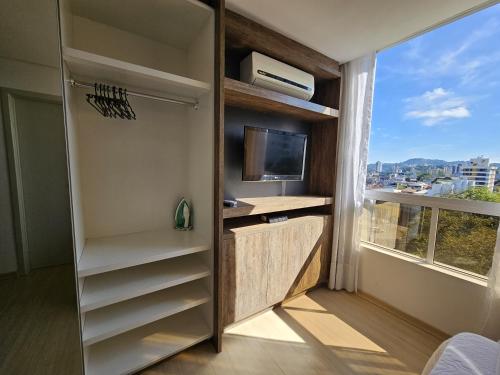 a room with a closet with a tv and a window at Loft Centro Oktoberfest - Blumenau in Blumenau