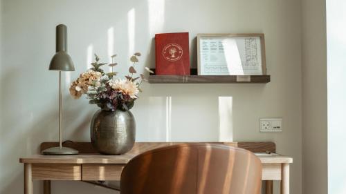a desk with a vase of flowers and a lamp at Arnbjerg Pavillonen in Varde