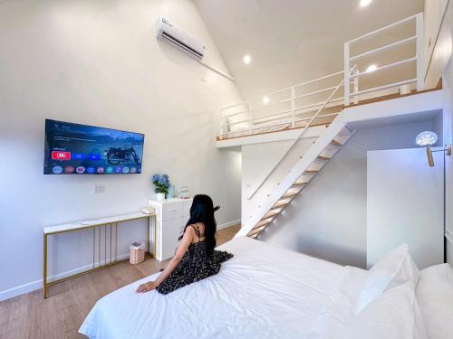 a woman sitting on a bed in a room with a staircase at Britishhillresort สัตหีบ บางเสร่ ช่องเเสมสาร in Ban Tao Than