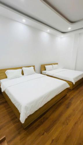 two beds in a white room with wooden floors at HOMESTAY Hoàng GIa in Ấp Ông Tú