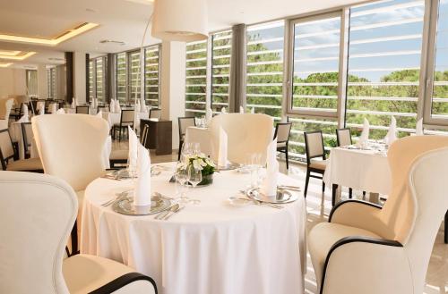 a restaurant with white tables and chairs and windows at Hotel Slovenija - Terme & Wellness LifeClass in Portorož