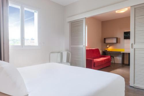 a bedroom with a white bed and a red chair at Westlodge Dardilly Lyon Nord in Dardilly