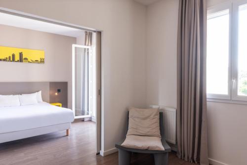 a bedroom with a bed and a chair and a window at Westlodge Dardilly Lyon Nord in Dardilly