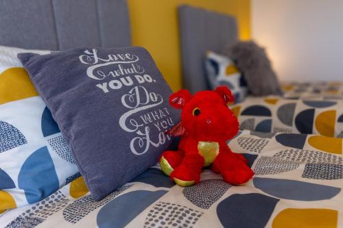 ein roter Teddybär sitzt auf einem Bett neben einem Kissen in der Unterkunft Cosy Dragons, Sherlock Holmes in Abergavenny