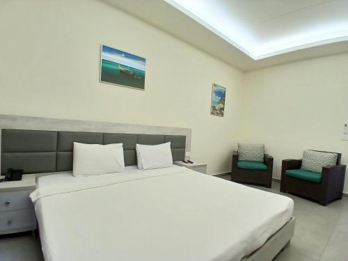 a bedroom with a large white bed and two chairs at Amchit Grand Hotel in Al Qarfī