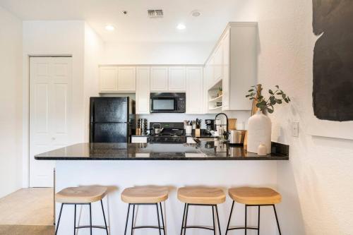Una cocina con gabinetes blancos y una encimera con taburetes. en Designer Desert Condo! Poolhot Tub Dogs Welcome!, en La Quinta
