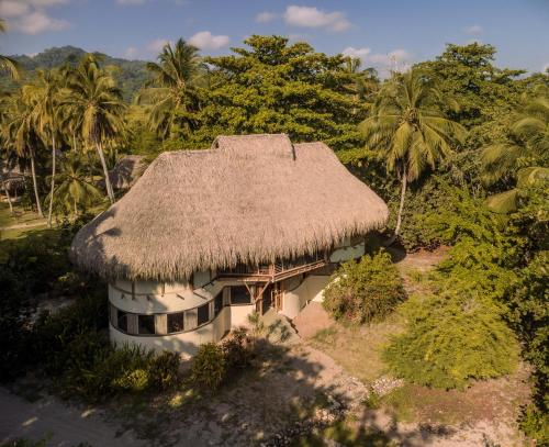 an old house with a straw roof and palm trees at Hotel Playa Bonita Tayrona in Buritaca