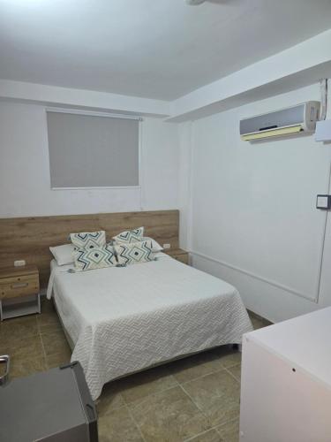 a bedroom with a bed with white sheets and blue pillows at Hotel Rodadero Dorado in Santa Marta