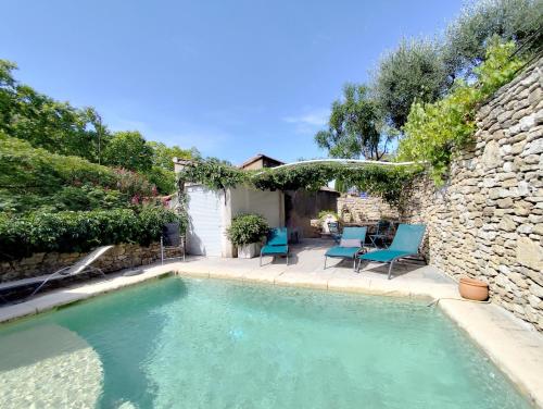 una piscina con sillas azules y una pared de piedra en Les trois gites, en Robion en Luberon
