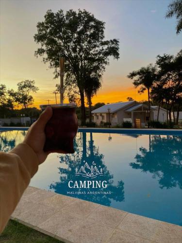a person holding a cup in front of a pool at Cabañas Camping Malvinas Argentinas in Paso de la Patria